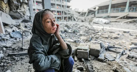 Palestinian children waiting for humanitarian aid amid destroyed buildings in Gaza during the ongoing humanitarian crisis in 2026.
