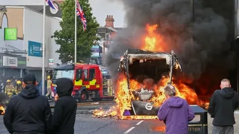 Police vehicles and crowds during unrest in Belfast as anti-immigration protests and riots escalate across city streets in 2026.