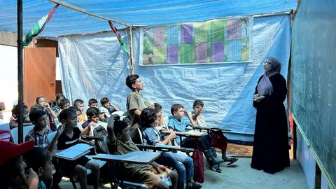 A displaced Palestinian student studying inside a damaged tent in Gaza amid the education crisis of 2026, with rubble visible in the background