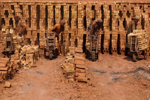 Brick kiln worker pushing wheelbarrow of bricks in Sheikhupura, Punjab, Pakistan
